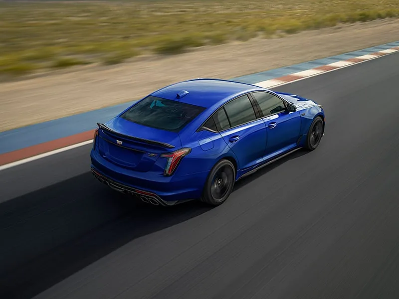 A blue Cadillac CT5-V Blackwing driving through a corner on a racetrack, seen from above and behind